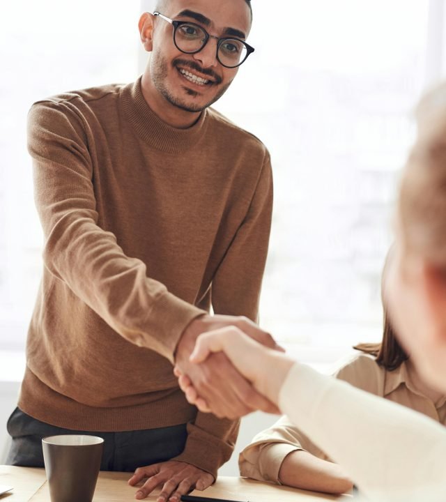 Smiling professionals engage in a welcoming handshake at a business meeting indoors.